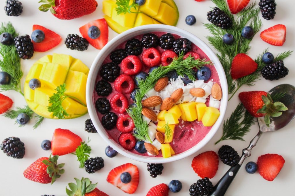 A bowl of fruit is surrounded by other fruits.